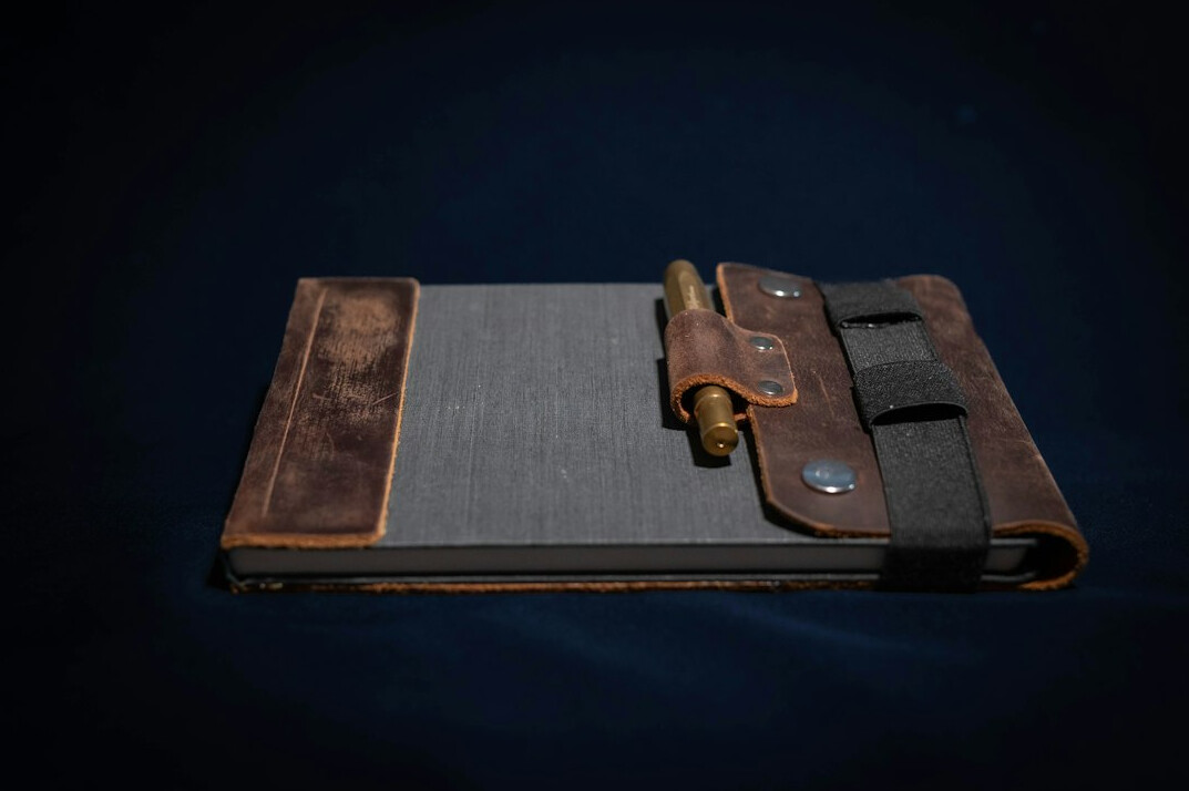 Open leather notebook with magnifying glass and vintage map on wooden desk